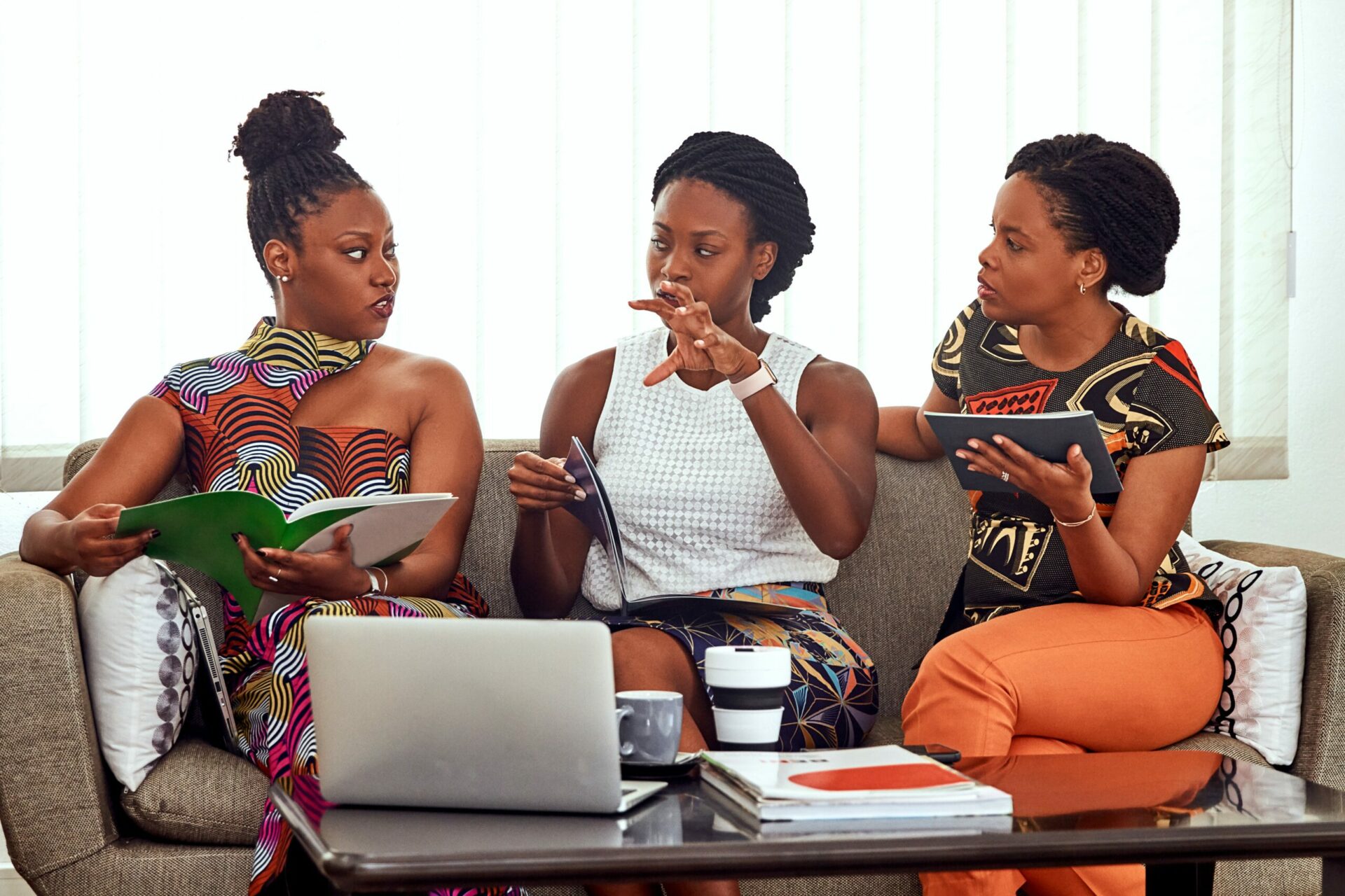 Three women in conversation with notebooks and a laptop.