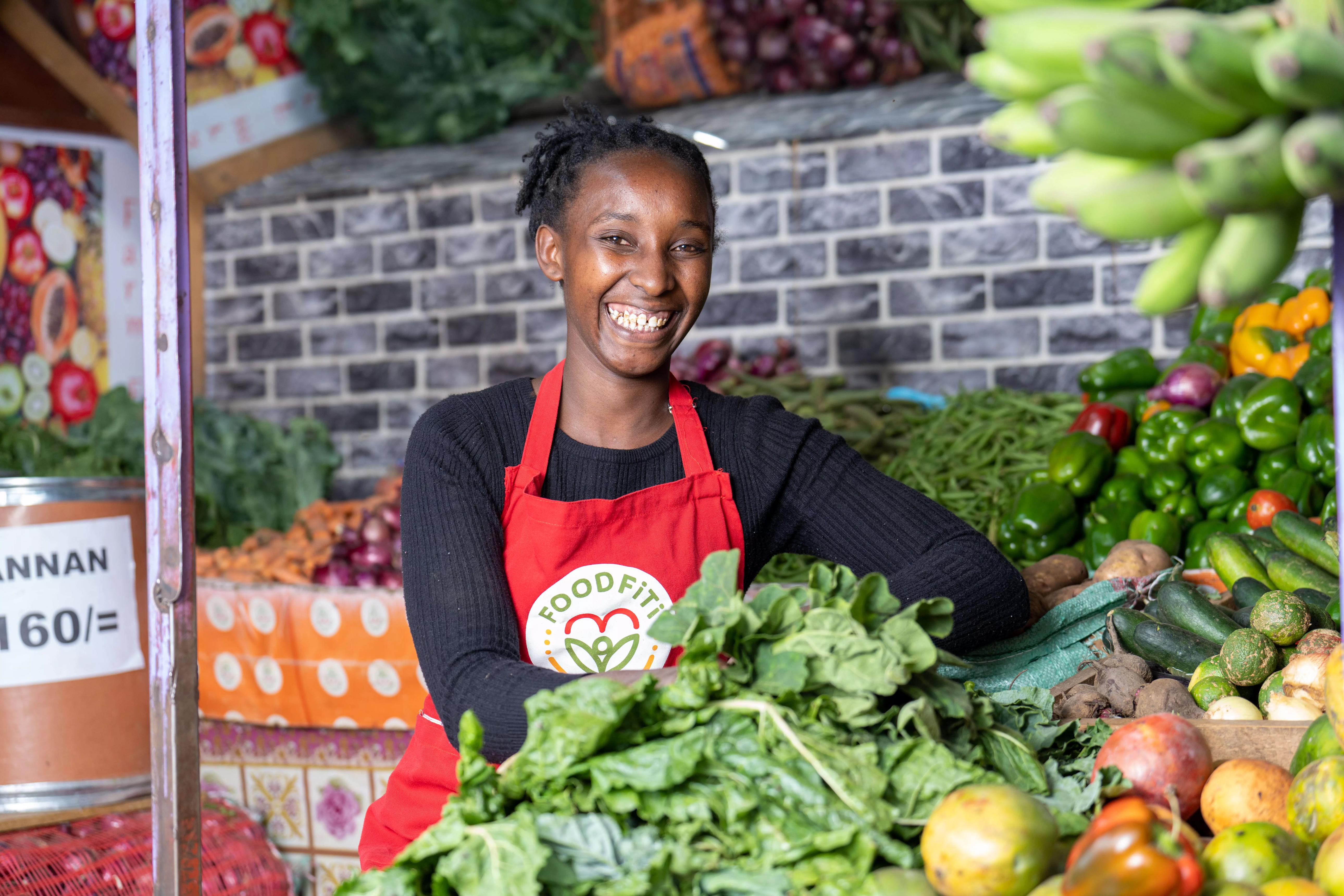 A smiling market trader surrounded by fresh produce.
