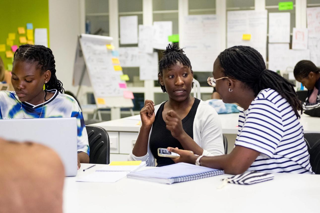 Young women discussing ideas around a table with laptops and notebooks.